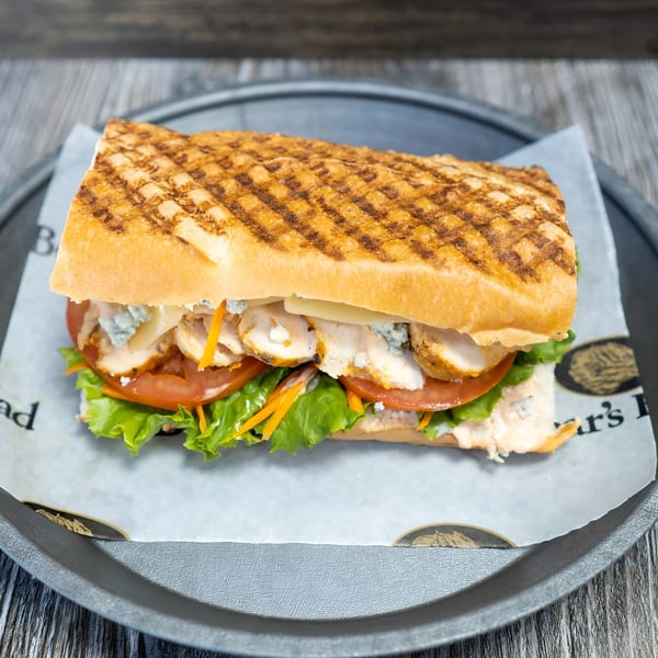 Grilled chicken panini with lettuce, tomato, cheese, and sauce on a dark plate.