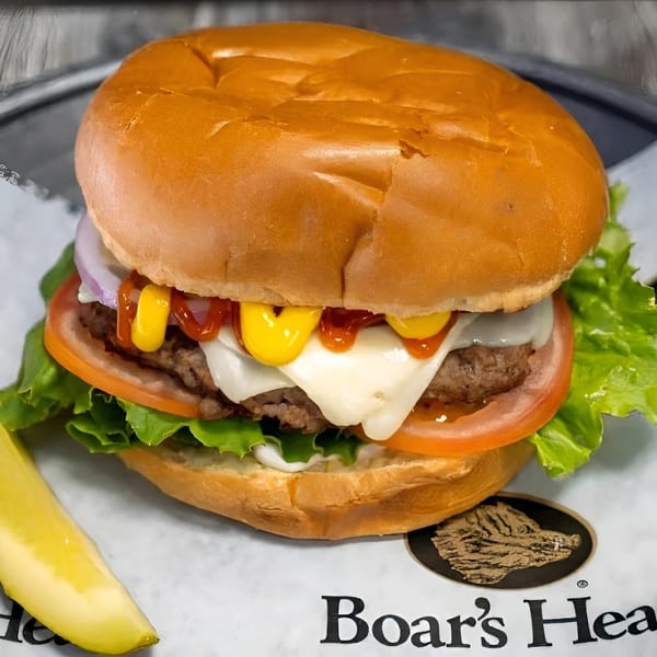 A juicy burger with melted cheese, lettuce, tomato, onion, ketchup, and mustard, with a pickle spear.