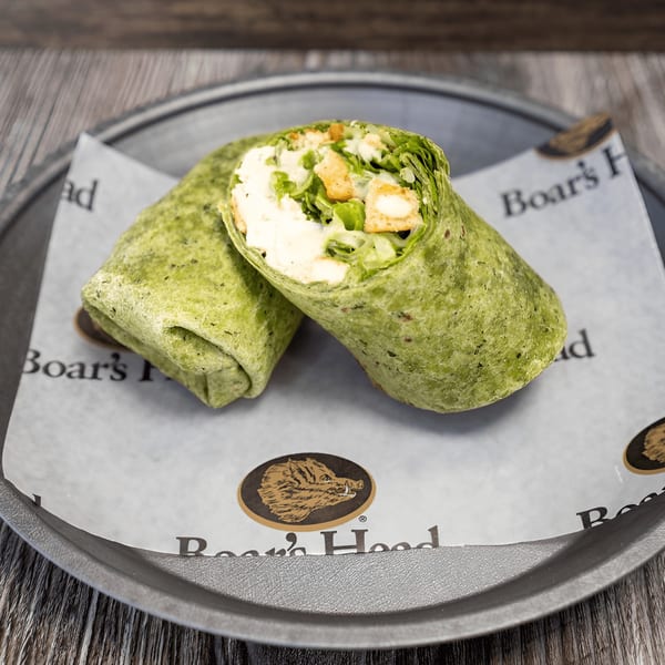 Two green spinach wraps, filled with chicken, lettuce, and white sauce, on a Boar's Head paper.