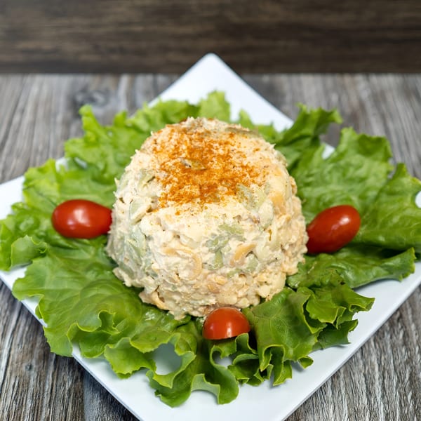 Chicken salad mound topped with paprika, surrounded by lettuce and cherry tomatoes on a white plate.