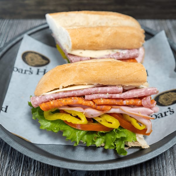 Two hearty American subs with meat, cheese, lettuce, tomatoes, and peppers on a tray.